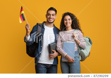 International Education. Middle Eastern Student Couple With Backpacks Holding German Flag International Education. Middle Eastern Student Couple With Backpacks Holding German Flag 87290209