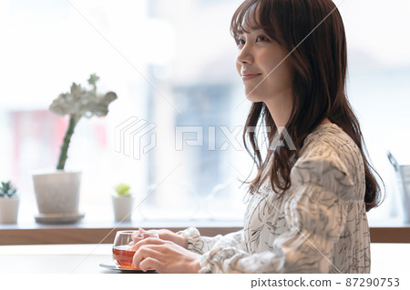 一位年輕女子在咖啡館靠窗的座位上喝茶 一位年輕女子在咖啡館靠窗的座位上喝茶 87290753