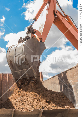 Excavation works. The bucket of the tractor loads the soil ground with a heavy shovel into the back of a dump truck on the construction site Excavation works. The bucket of the tractor loads the soil ground with a heavy shovel into the back of a dump truck on the construction site 87291317