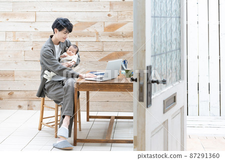 一個抱著嬰兒做遠程工作的年輕人 87291360