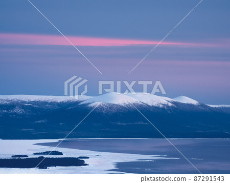 Snow-covered polar cone hills in winter early in the morning. Winter polaris landscape. View of the snow-covered hills and White sea. Cold winter weather. Harsh northern climate background. Snow-covered polar cone hills in winter early in the morning. Winter polaris landscape. View of the snow-covered hills and White sea. Cold winter weather. Harsh northern climate background. 87291543