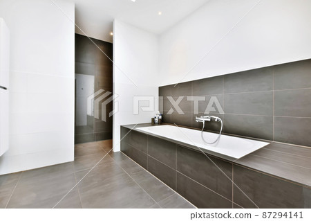 The bathroom is in a minimalist style with a comfortable bathtub and a dark tiled floor 87294141