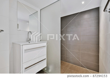 The bathroom is in a minimalist style with a white chest of drawers and a mirror 87294153