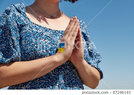 Ukrainian woman with a flag symbol on her hand prays against the blue sky. Stop war Ukrainian woman with a flag symbol on her hand prays against the blue sky. Stop war 87296193
