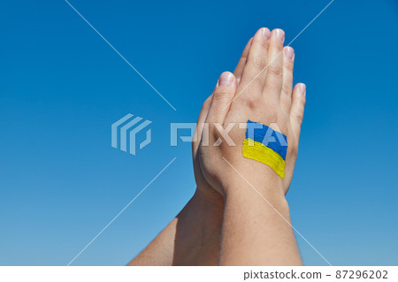 Womans hands with ukrainian flag symbol prays against the blue sky. Stop war 87296202