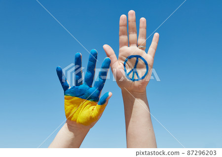 Females hand painted in ukrainian flag colors and peace sign against blue sky. Stop the war 87296203