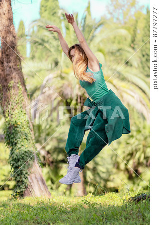 Hiphop girl in emerald outfit in pose flies in a jump in a green park on a summer day 87297277