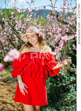 Cheerful girl posing in a red dress in spring blooming garde 87297360