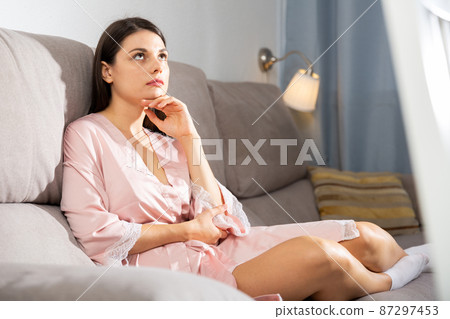 Disappointed girl sitting on sofa in living room Disappointed girl sitting on sofa in living room 87297453