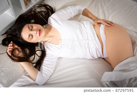 Young woman in white sleepwear sleeping in bed in home Young woman in white sleepwear sleeping in bed in home 87297591