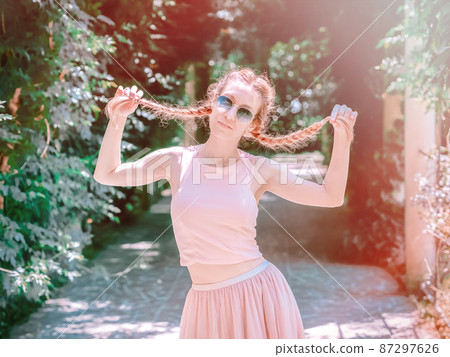 Lady holding herself for pigtails while standing in a green park on a summer day. Posterization 87297626