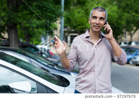 Portrait of male who is standing satisfied near his car and talking by phone Portrait of male who is standing satisfied near his car and talking by phone 87297678