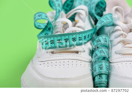 Centimeter in cyan blue color curled on white trainers, closeup 87297702