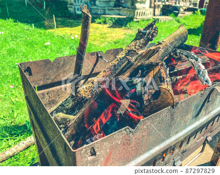 brazier with smoldering wooden firewood. a small, metal, rusty brazier for cooking shish kebabs. tongues of flame in an enclosed space. cooking food 87297829