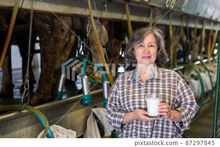 Elderly female with glass of cow milk in milking parlor 87297845