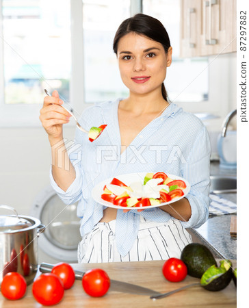 Housewife prepares tomato and avocado salad in the kitchen 87297882