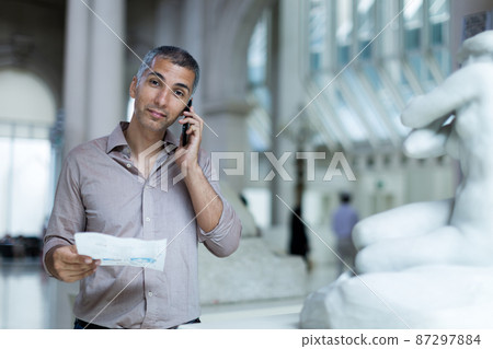 Adult male is visiting at the exposition with brochure and talking by phone Adult male is visiting at the exposition with brochure and talking by phone 87297884