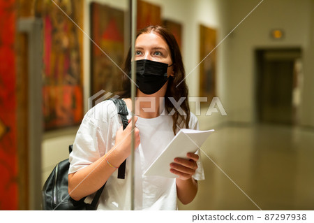 Interested girl in a protective mask in the museum, looks at the exhibit located behind the glass 87297938