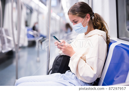 Young woman in mask with mobile phone traveling by train on subway Young woman in mask with mobile phone traveling by train on subway 87297957