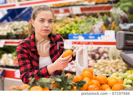 Portrait of young woman buying tangerines at grocery store Portrait of young woman buying tangerines at grocery store 87297986