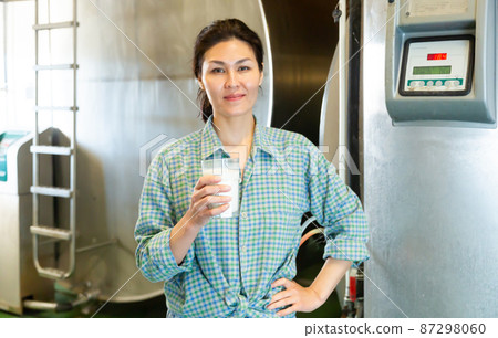 Portrait of a smiling asian woman standing in a dairy farm with a glass of milk 87298060