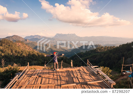 Cheerful asian man standing and enjoying the mountain view from balcony viewpoint in the evening at countryside 87298207