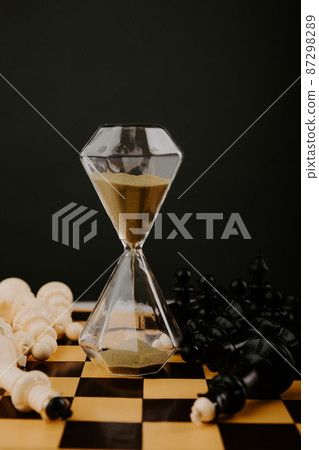 Hourglass with gold sand and chessboard on a dark background. Strategy, management or leadership concept. Vertical image Hourglass with gold sand and chessboard on a dark background. Strategy, management or leadership concept. Vertical image 87298289