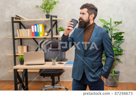 handsome mature entrepreneur in jacket having coffee break with cup at office, success 87298673