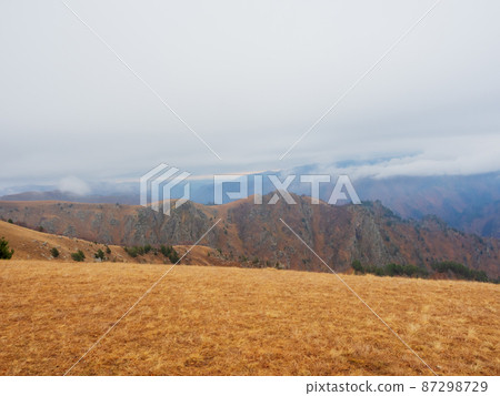 Autumn golden field located in the highlands with white clouds descending to the peaks. 87298729