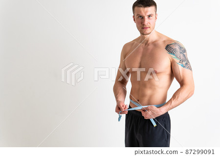 A man measures the waist of a metre and poses against a white background isolated fit muscular background, healthy female bodybuilding woman weight, healthy Oss nutrition athlete, adult sport A man measures the waist of a metre and poses against a white background isolated fit muscular background, healthy female bodybuilding woman weight, healthy Oss nutrition athlete, adult sport 87299091