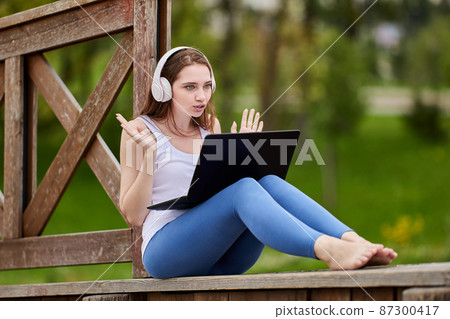 Web conference on nature by woman in cordless headphones with laptop. 87300417