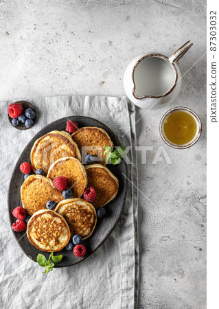 Pancakes in ceramic plate with berries, mint leaves, gravy boats on linen napkin, top view 87303032