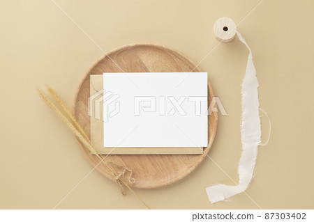 Blank greeting card invitation Mockup on Brown envelope with Dried bunny tails grass on beige background, Minimal table workplace composition, flat lay, mockup 87303402