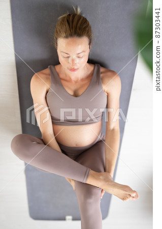 Young beautiful pregnant woman training pilates at home in her living room. Healthy lifestyle and active pregnancy and motherhood concept. Young beautiful pregnant woman training pilates at home in her living room. Healthy lifestyle and active pregnancy and motherhood concept. 87303441