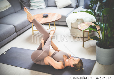 Young beautiful pregnant woman training pilates at home in her living room. Healthy lifestyle and active pregnancy and motherhood concept. Young beautiful pregnant woman training pilates at home in her living room. Healthy lifestyle and active pregnancy and motherhood concept. 87303442
