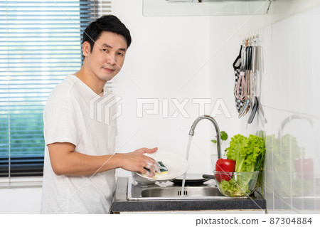 happy man washing dishes in the sink in the kitchen at home 87304884