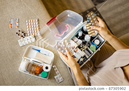 Closeup female hand placing medicament domestic first aid kit. Storage organization emergency supply 87305902