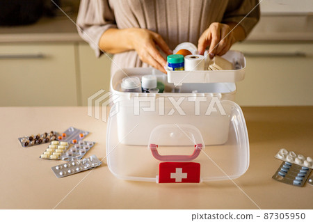 Closeup female hand placing medicament domestic first aid kit. Storage organization emergency supply Closeup female hand placing medicament domestic first aid kit. Storage organization emergency supply 87305950