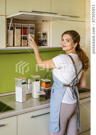 Laughing young female housewife posing during general cleaning, tidying up in cupboard kitchen Laughing young female housewife posing during general cleaning, tidying up in cupboard kitchen 87305951