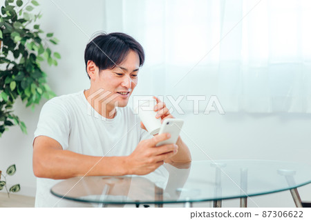一個男人在房間裡看智能手機（微笑） 87306622