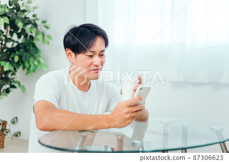 A man looking at a smartphone in the room (smile) 87306623