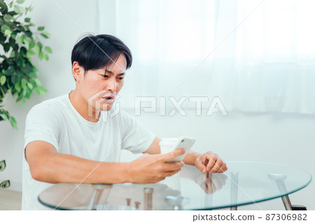 一個男人在房間裡看智能手機(驚訝) 一個男人在房間裡看智能手機(驚訝) 87306982