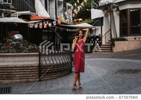 Beautiful sexy brunette girl in a red dress posing on street with paving stones in Italy 87307060