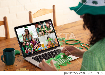 Mixed race woman in costume making st patrick's day video call to friends on laptop at home Mixed race woman in costume making st patrick's day video call to friends on laptop at home 87308918