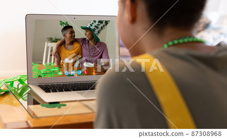 Mixed race woman making st patrick's day video call to friends holding beers on laptop at home Mixed race woman making st patrick's day video call to friends holding beers on laptop at home 87308968