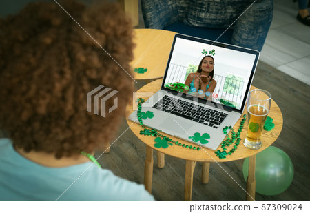 Mixed race man at bar making st patrick's day video call to woman blowing kiss on laptop screen Mixed race man at bar making st patrick's day video call to woman blowing kiss on laptop screen 87309024