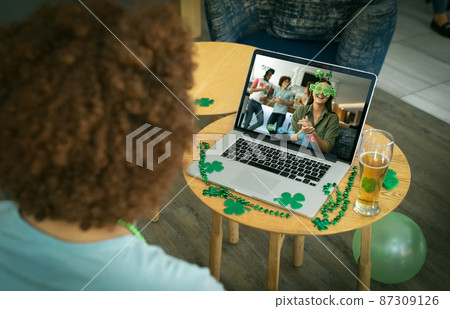 Mixed race man at bar making st patrick's day video call to friends on laptop Mixed race man at bar making st patrick's day video call to friends on laptop 87309126
