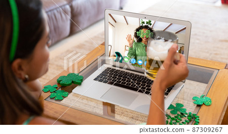 Caucasian woman holding beer having st patrick's day video call with friend on laptop at home Caucasian woman holding beer having st patrick's day video call with friend on laptop at home 87309267