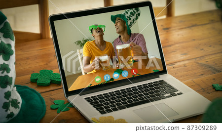 Two mixed race male friends with beers making st patrick's day video call on laptop screen at home 87309289