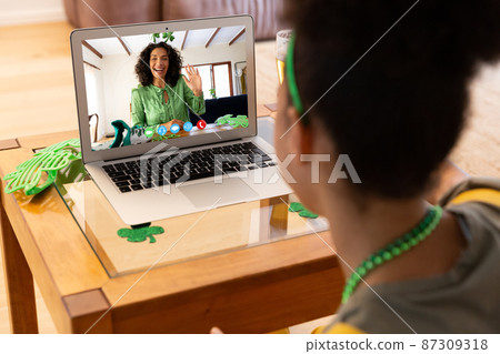 Mixed race woman in making st patrick's day video call to waving female friend on laptop at home Mixed race woman in making st patrick's day video call to waving female friend on laptop at home 87309318